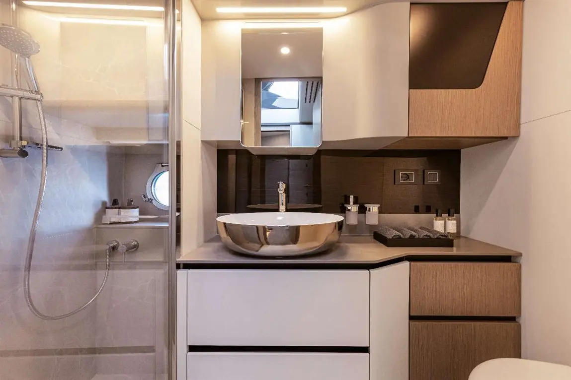 Modern bathroom featuring a round sink, wooden cabinets, shower with glass door, and stylish toiletries on the countertop.